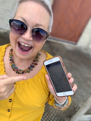 Leslie in sunglasses pointing excitedly at her cell phone