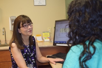 Doctor Basler sits at computer and talks compassionately with a brown-haired patient. 