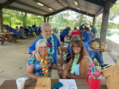 Three women wearing leis build birdhouses at the 2023 Camp Bluebird held at Tombigbee State Park