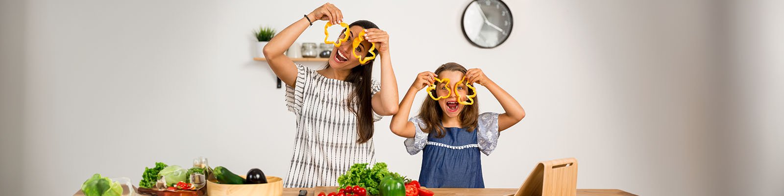 a mom and daughter posing with bell pepper slices like glasses in front of a table full of vegetables