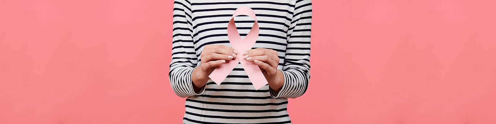 Woman in striped shirt holding a pink ribbon on a pink background