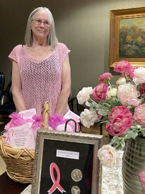 Carol Pierson stands with framed Breast Cancer Advocate award, balloons and a basket of Knitted Knoc