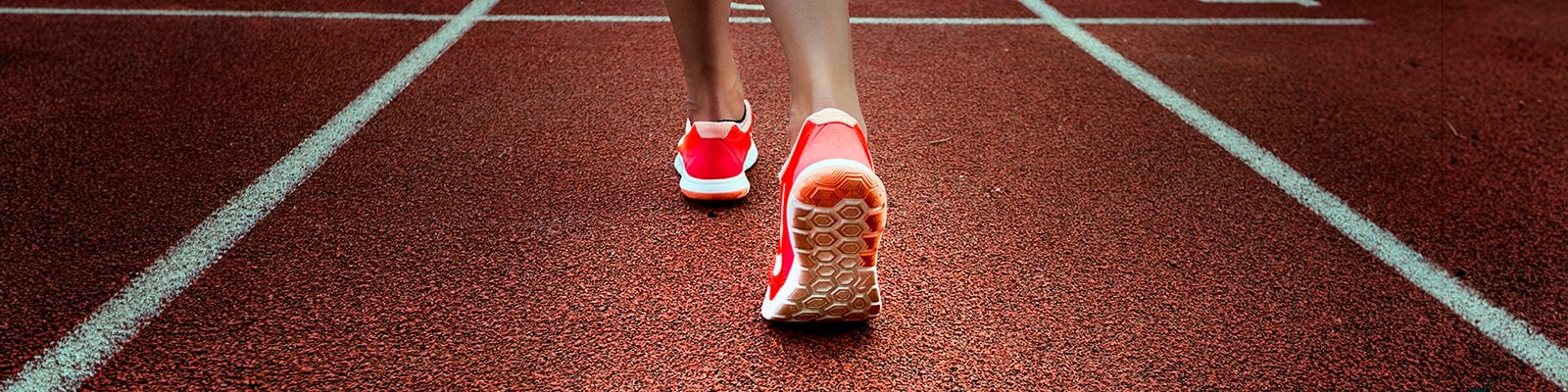 an African-American woman's ankles and feet wearing bright red running shoes on a running track